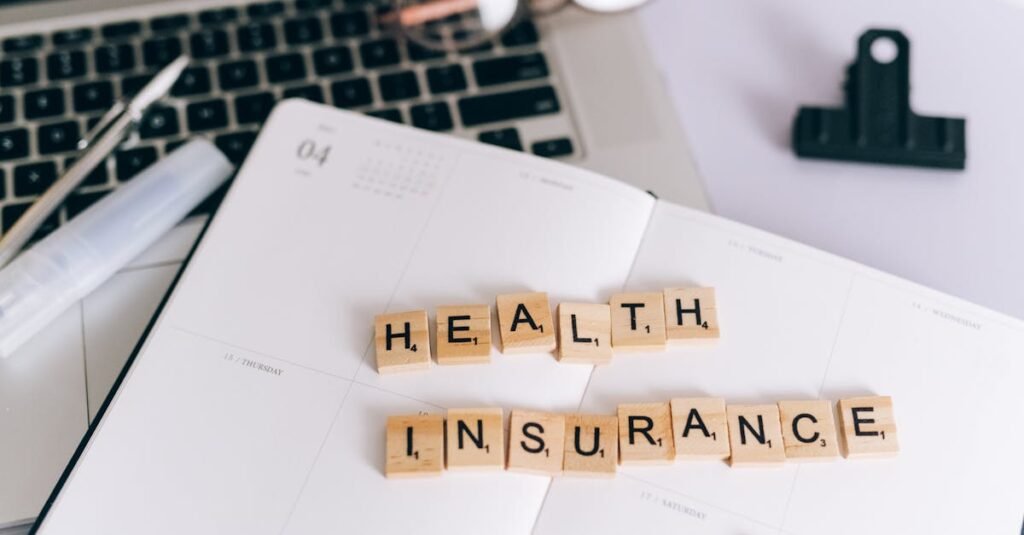 Close-up of Scrabble tiles spelling 'Health Insurance' on a planner with a laptop.