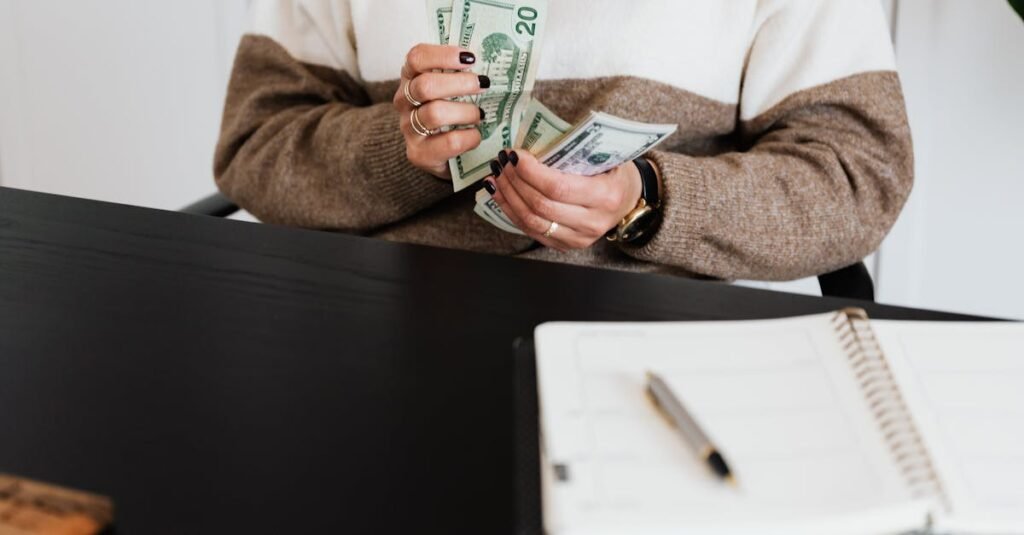 Close-up of an adult counting dollar bills at a desk with a notebook.